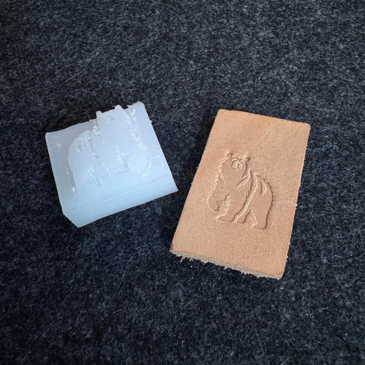 White plastic stamp and brown leather sample with embossed bear design on leather