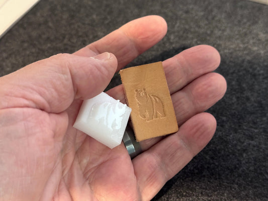 Hand holding a white plastic stamp and brown leather sample with embossed bear design on leather