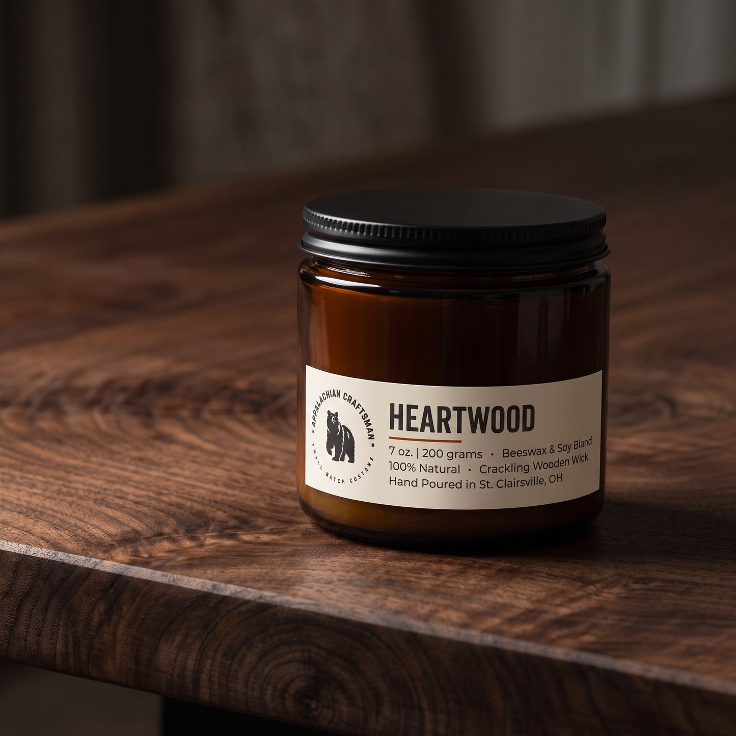 An amber glass jar candle with a black lid and a white label reading 'Heartwood' sits on a dark wooden table.